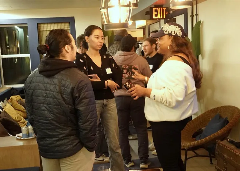 Three attendees chatting in a small-group candid at an AI Build Club event, March 2026